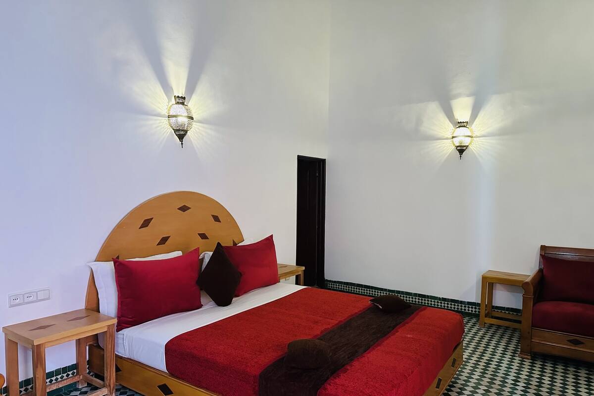 A neatly arranged hotel room with a bed, two nightstands, a chair, and a wall-mounted light fixture.