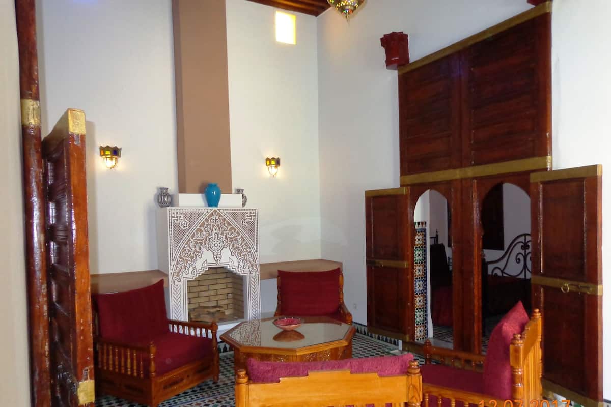 A traditional Moroccan room with a wooden sofa, a small round table, a decorative wall piece, and a tiled floor.