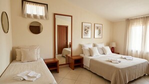 Habitación de hotel con dos camas, un espejo, una ventana con cortinas y obras de arte enmarcadas en la pared.