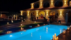 Una piscina con velas, un edificio con arcos y mesas al aire libre.