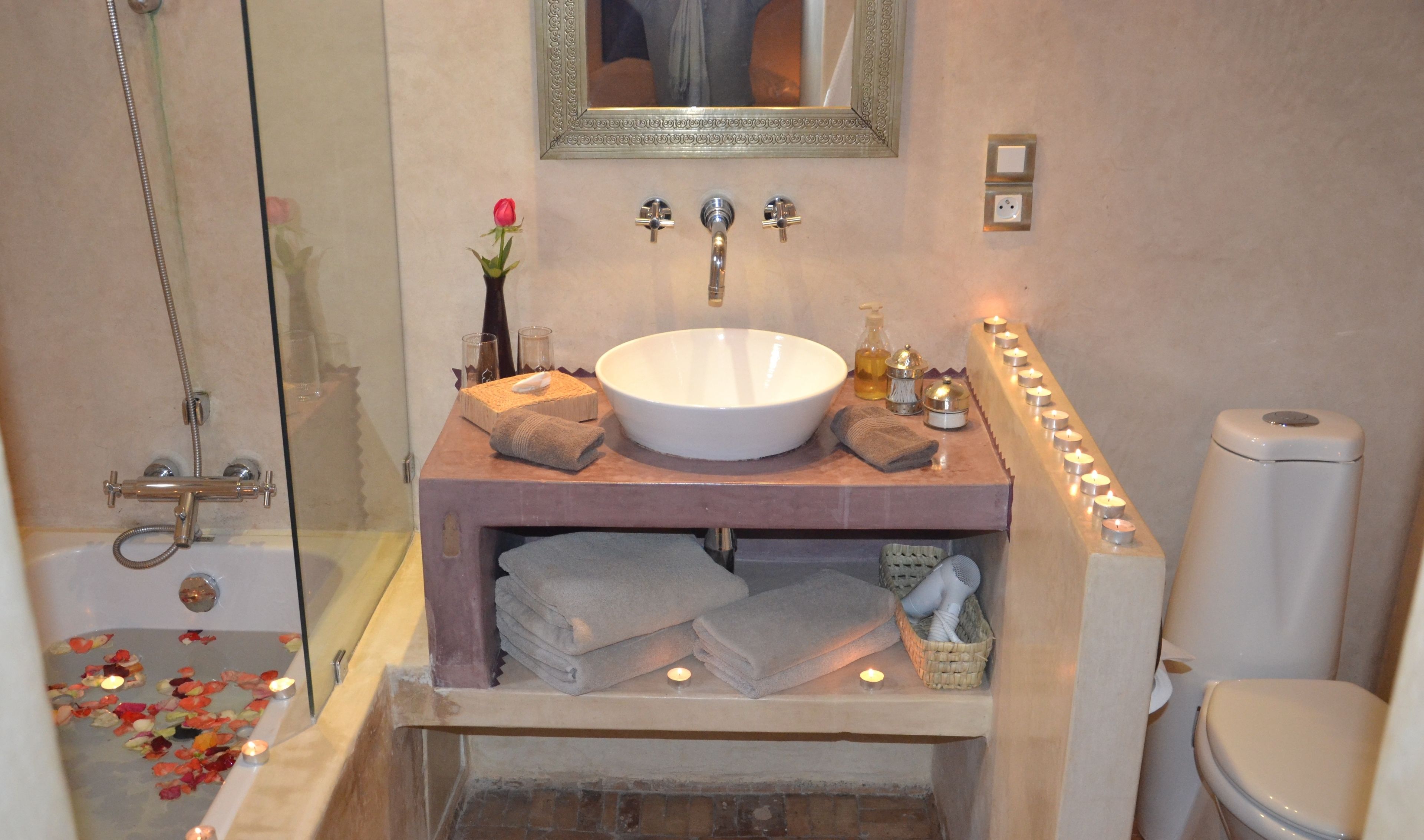 A bathroom with a large bathtub, a sink, and a toilet. There are towels and a vase with a flower on the sink counter.