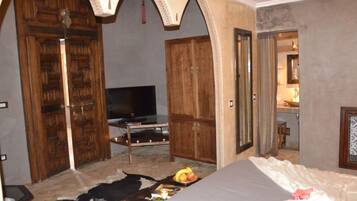 A room with a bed, a TV, wooden doors, and a small table with fruit.