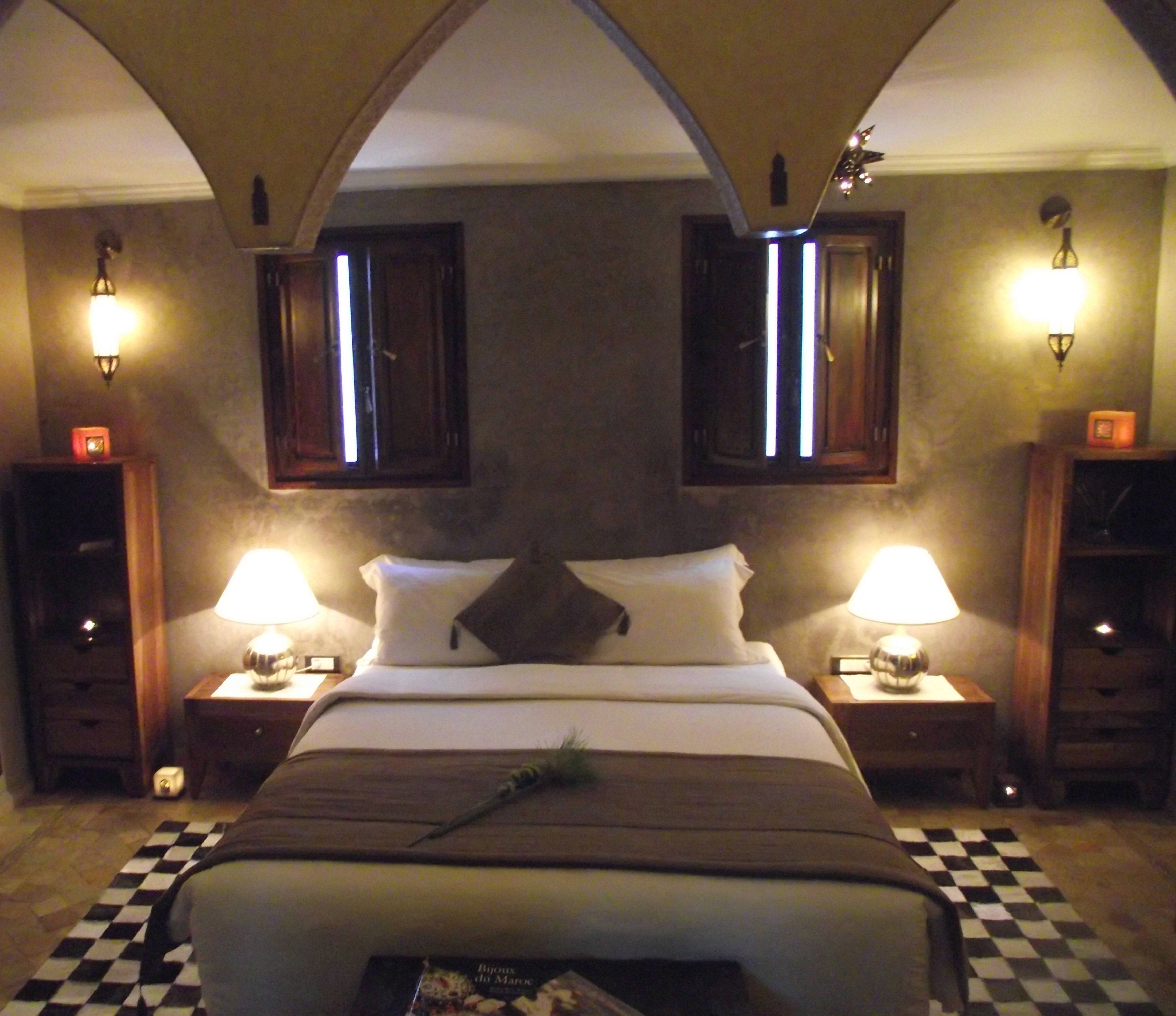 Habitación de hotel con una cama grande, dos mesitas de noche con lámparas, piso a cuadros y un elemento decorativo en la pared.