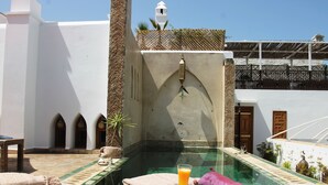 A pool area with a clear view of the pool, a glass of orange juice, and a towel. - Riad Kalaa (Rabat)