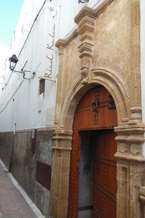 A historic building with a wooden door, stone columns, and a white wall with a sign.