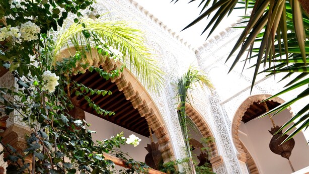 An ornate architectural structure with arches and intricate designs, featuring lush greenery and white flowers. - Riad Kalaa (Rabat)