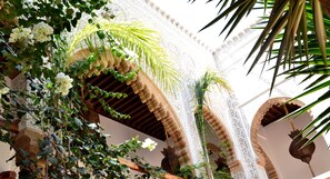 An ornate architectural structure with arches and intricate designs, featuring lush greenery and white flowers.