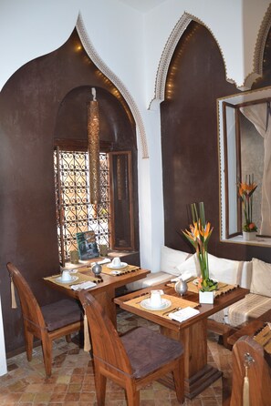 Un comedor con una mesa y sillas de madera, un jarrón decorativo con flores y una ventana con reja de metal.