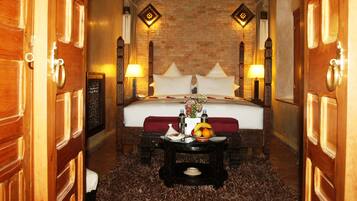 A hotel room with a large bed, wooden doors, a brick wall, and two wall-mounted lamps.