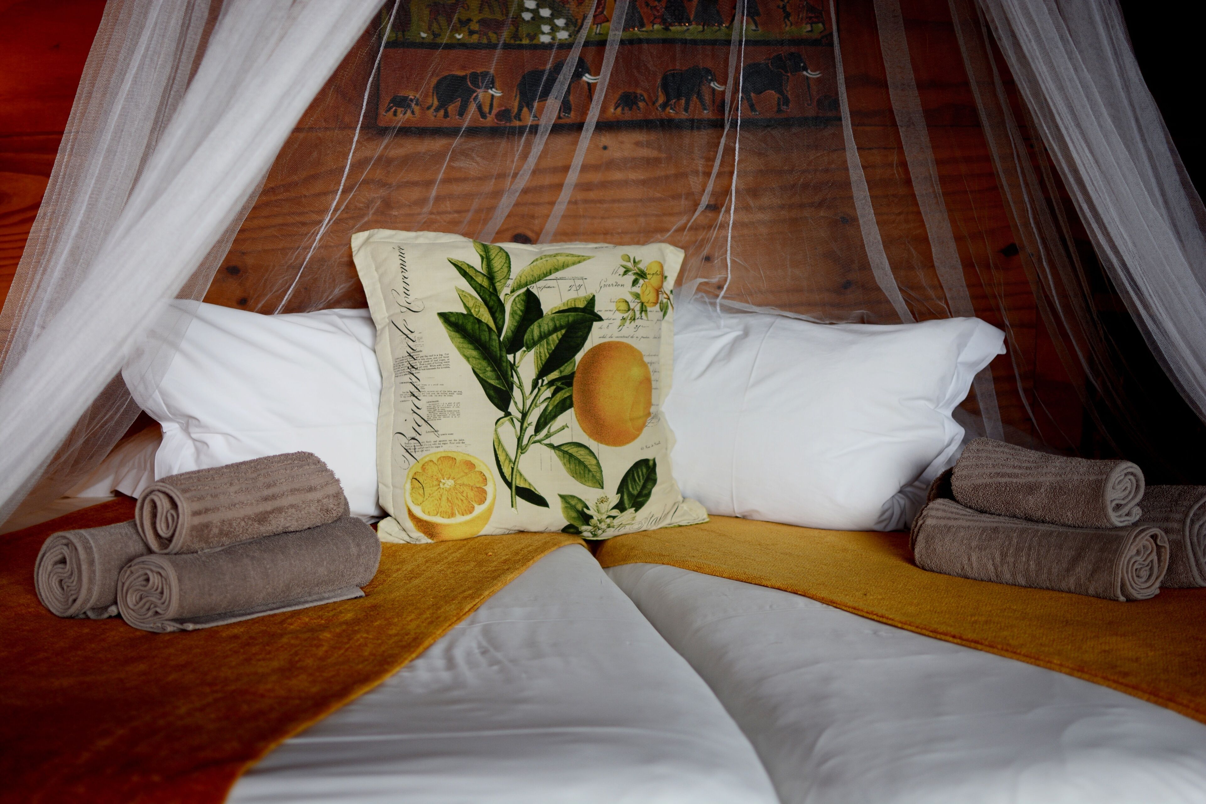 Een bed met witte lakens, een kussen met een fruitprint en opgerolde handdoeken.