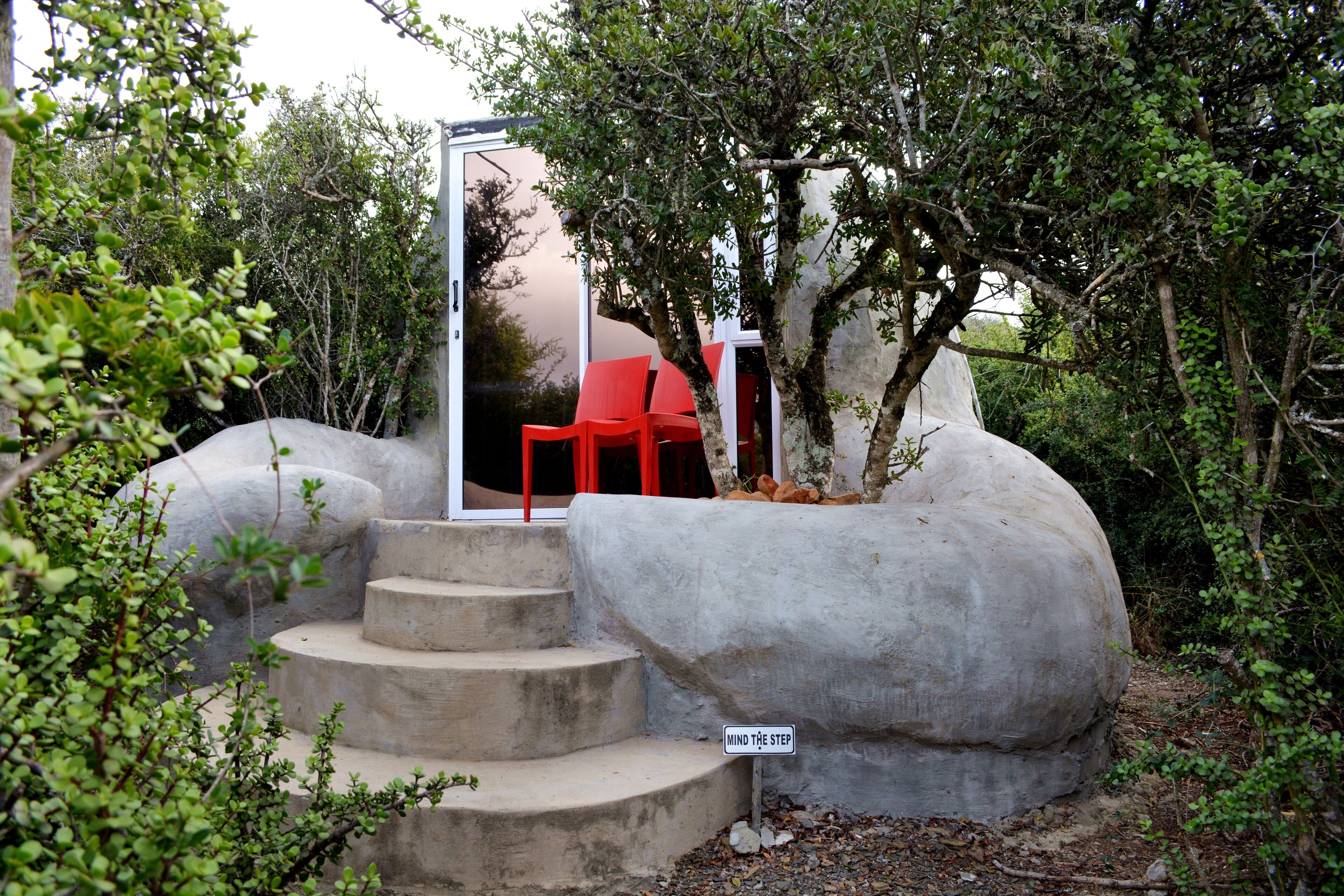 A concrete structure with steps leading to a red chair, surrounded by greenery.