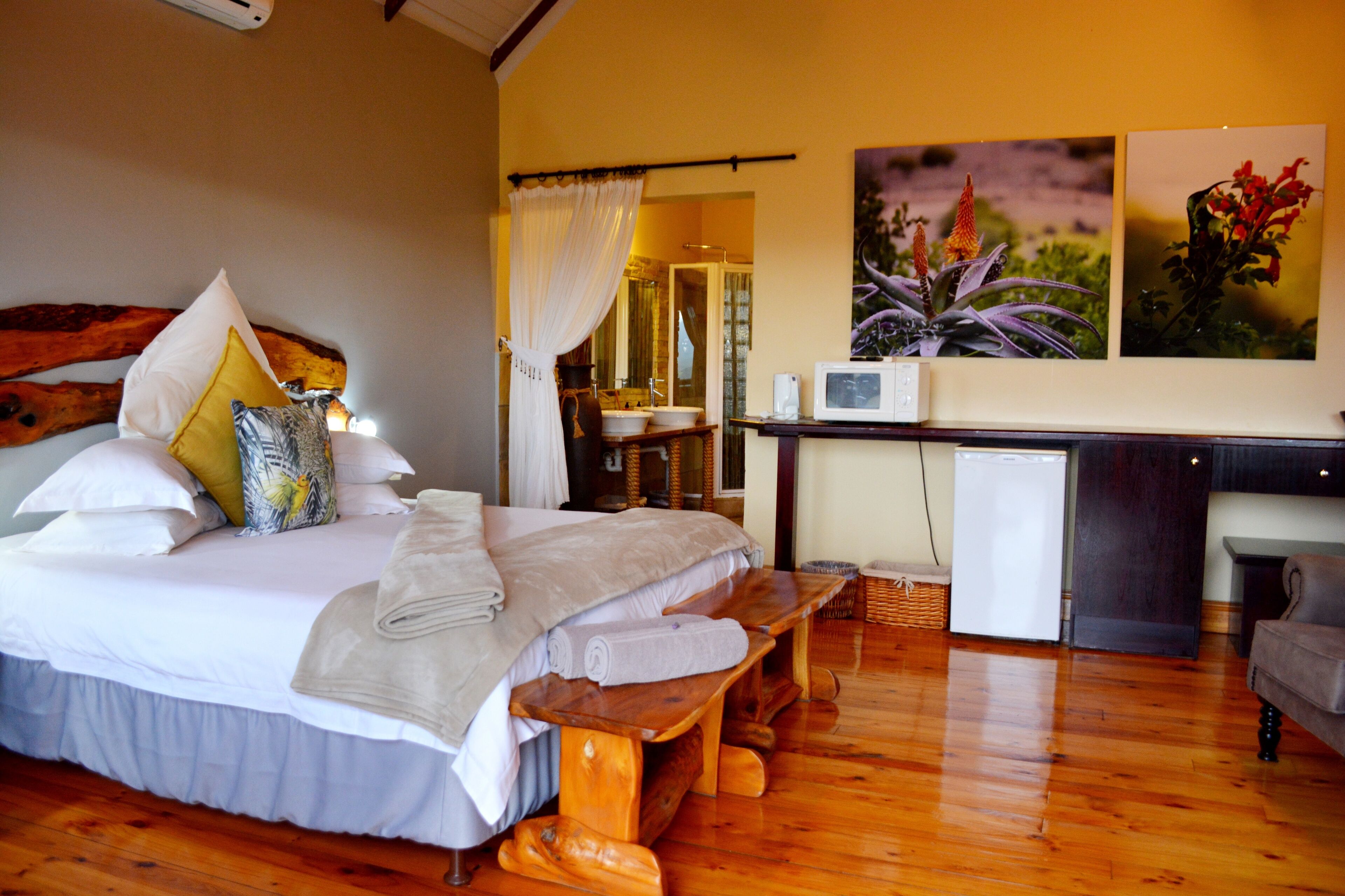 A bedroom with a large bed, a wooden bench, a small refrigerator, and a sink.