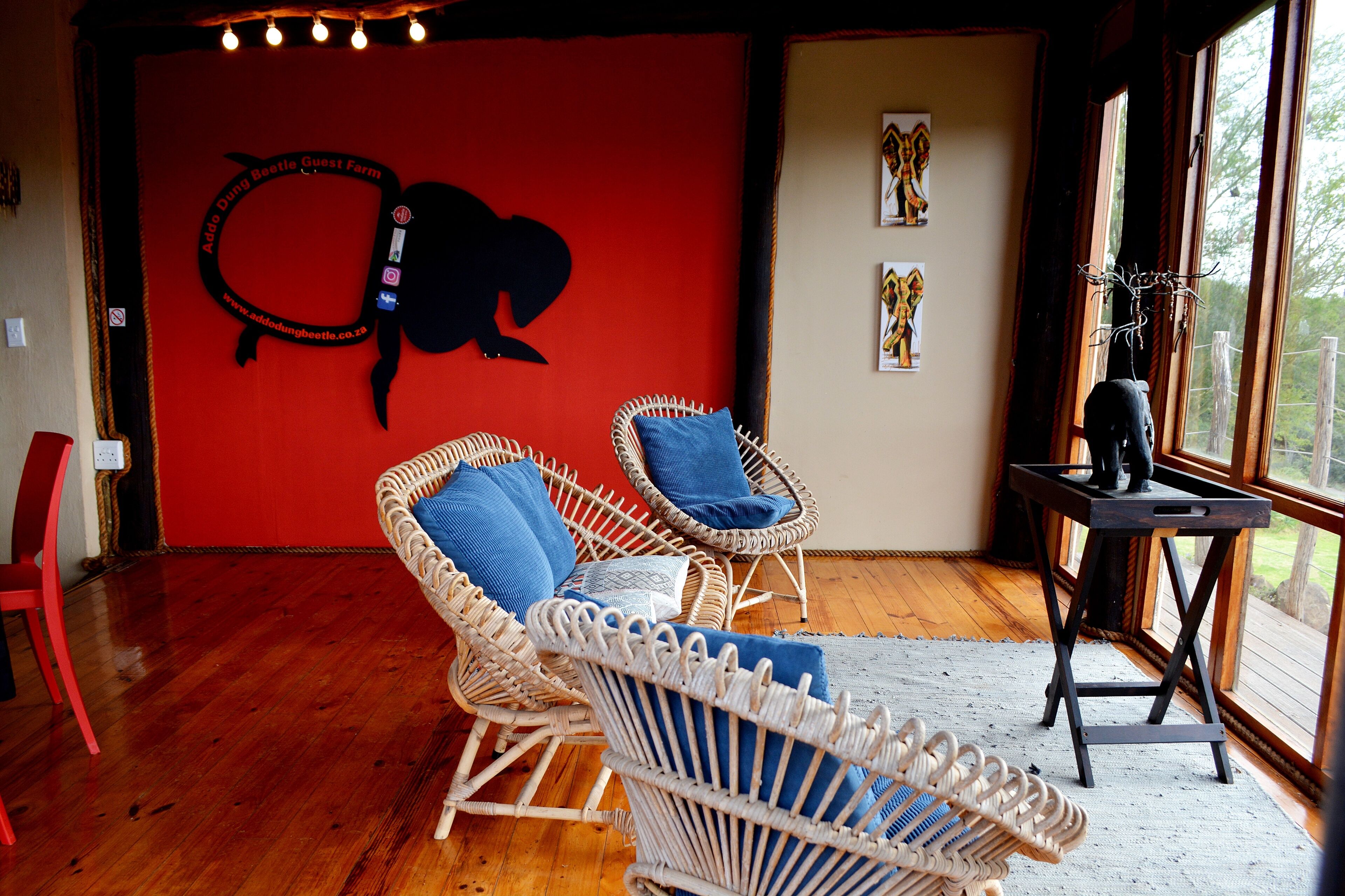 Une pièce avec des chaises en osier, un mur rouge et des œuvres d’art.