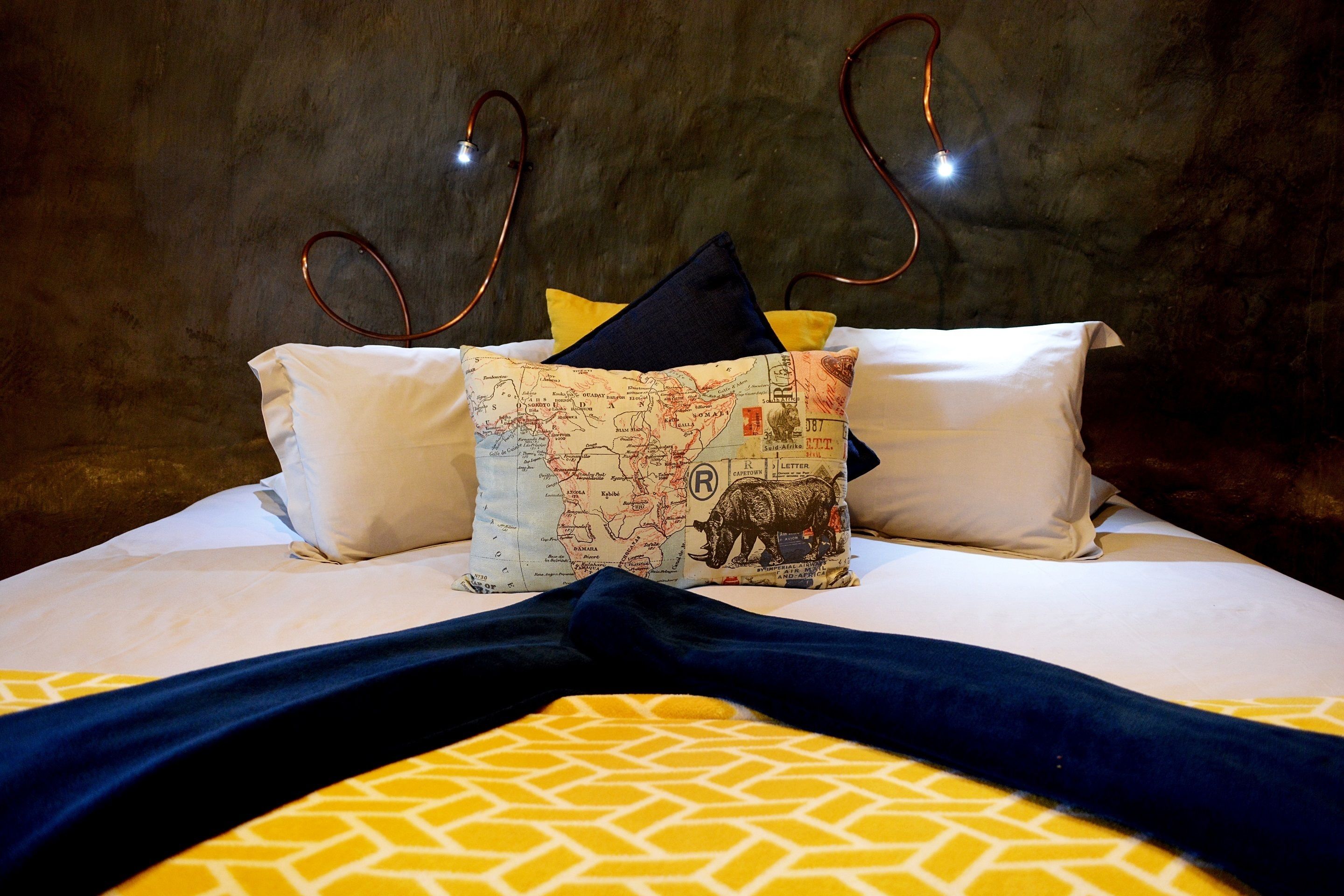 Una cama con ropa de cama de diseño blanco y amarillo, un plaid azul oscuro y almohadones decorativos, incluyendo uno con un diseño de mapa.