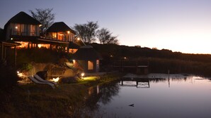 A lakeside property with a house, a dock, and a lounge chair by the water. - Addo Dung Beetle Guest Farm (Addo)