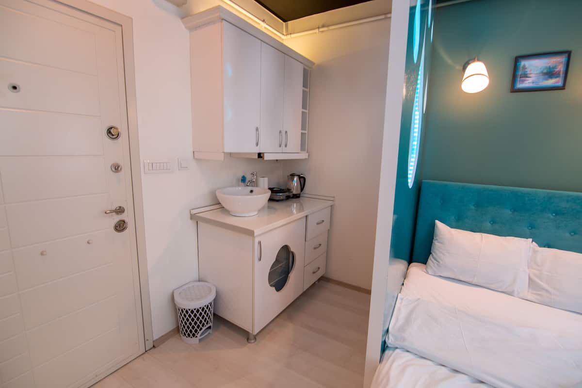 A compact bedroom with a bed, a small bathroom with a sink and cabinets, and a door.