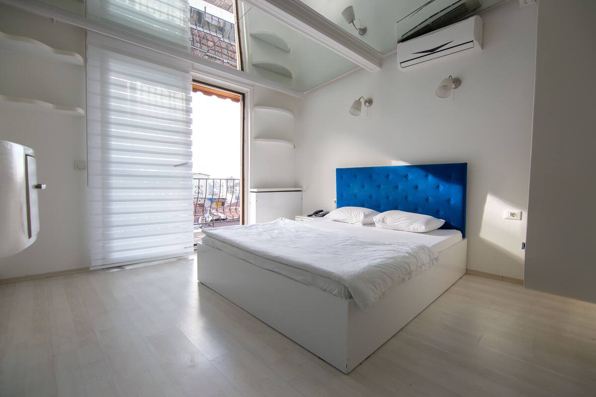 A bedroom with a large bed, a balcony, and an air conditioning unit.