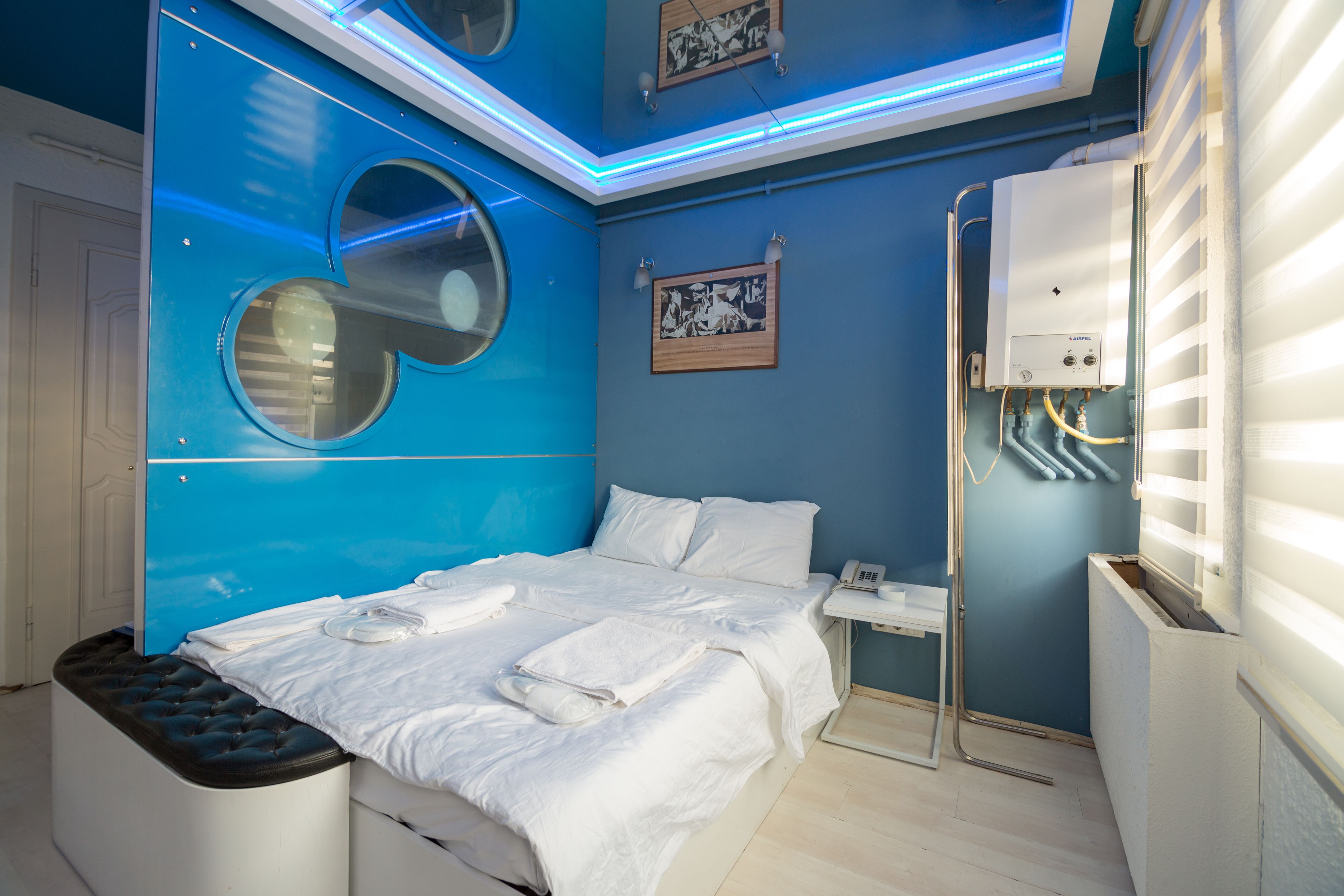 Moderni hotellihuone, jossa on suuri sänky, pieni yöpöytä, seinään kiinnitetty lämmitin ja ikkuna, jossa on sälekaihtimet.