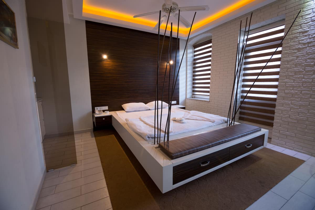 A modern bedroom with a large bed, a nightstand, a ceiling fan, and a window with blinds.