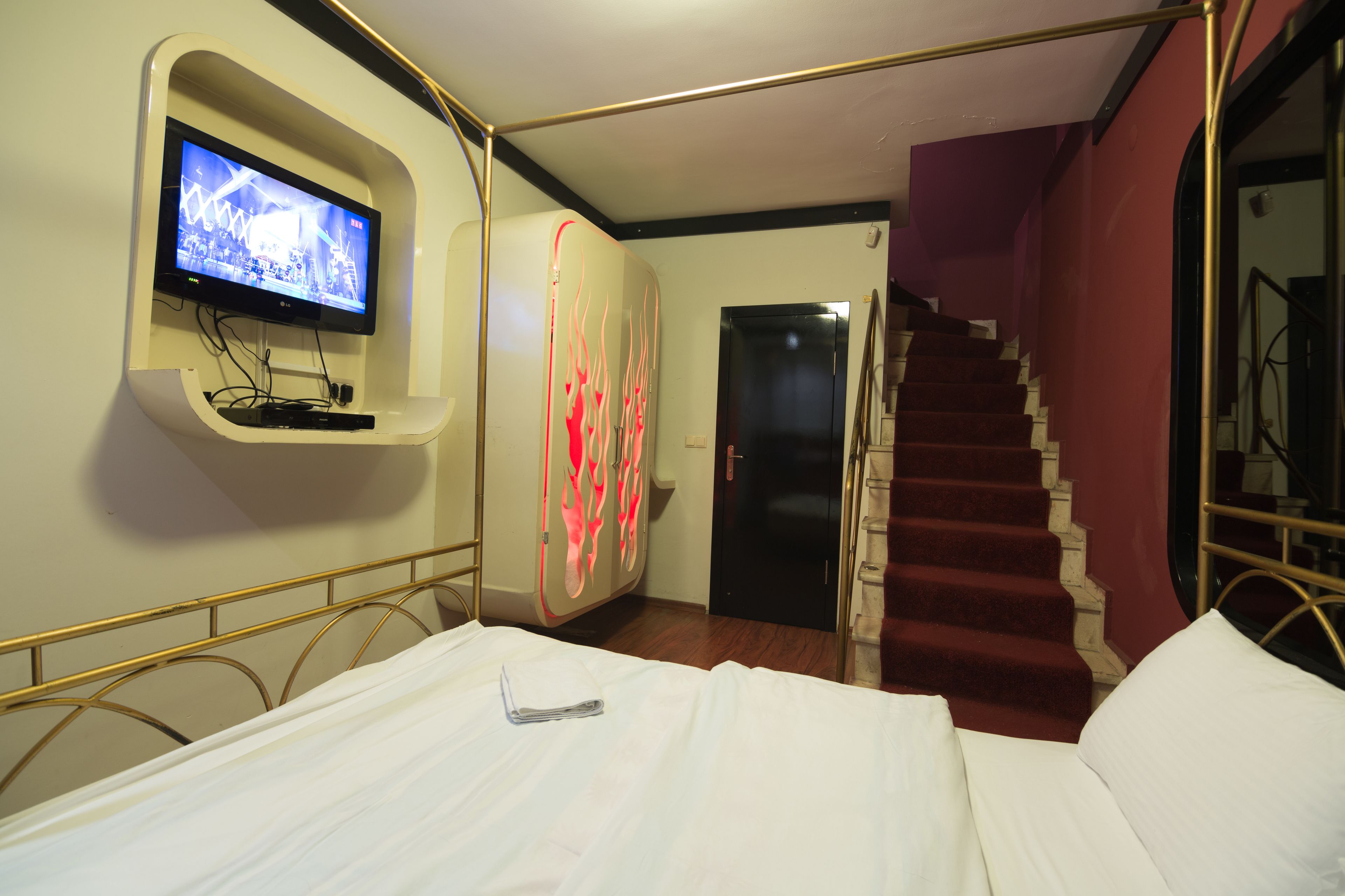A hotel room with a bed, a television mounted on the wall, a staircase, and a door.