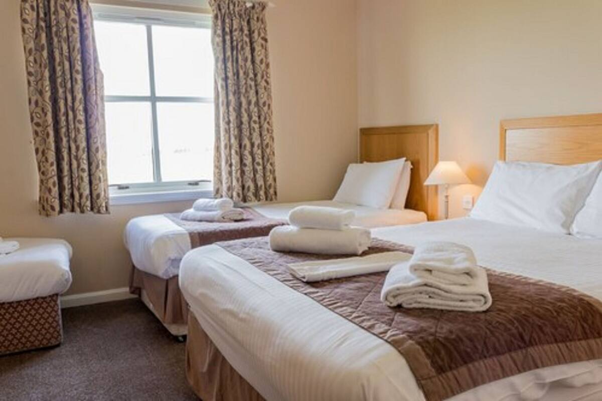 Una habitación de hotel con dos camas individuales, una cama más grande y una pequeña zona de estar.
