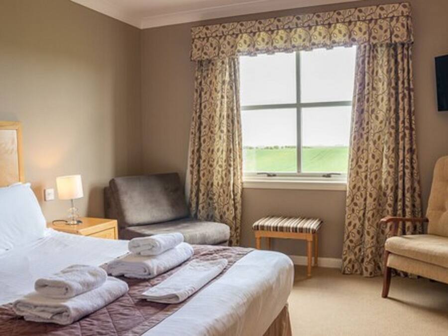 Una habitación de hotel con una cama, dos sillones, una mesita y una ventana con cortinas.