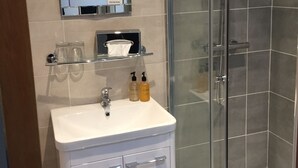 A modern bathroom with a glass shower enclosure, a white sink with a mirror above it, and toiletries on the sink. - Purdy Lodge (Belford)