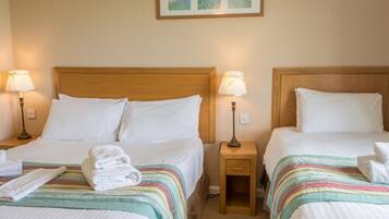 A hotel room with two beds, each with a wooden headboard, white linens, and striped blankets. There are bedside lamps and a framed picture on the wall.
