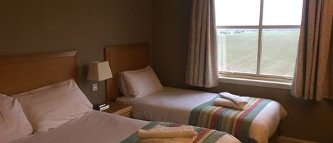 A hotel room with two beds, a nightstand with a lamp, and a window with curtains.