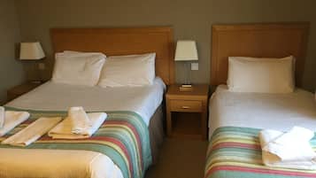 Two double beds with white linens, a wooden headboard, and a bedside table with a lamp.