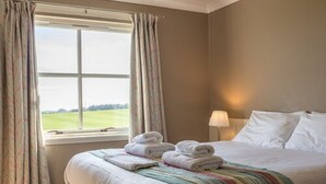 A hotel room with a bed, a window with curtains, and a view of a green landscape. - Purdy Lodge (Belford)