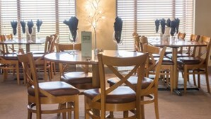 A dining area with round tables and wooden chairs, a central decorative tree, and a menu stand. - Purdy Lodge (Belford)