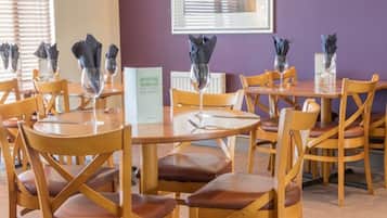 A dining area with round tables and wooden chairs, each with a glass and napkin holder.
