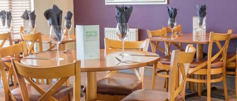 Un comedor con mesas redondas y sillas de madera, cada una con un portavasos y un sujetavasos.