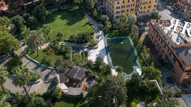 An aerial view of a coastal cityscape with a prominent building featuring a rooftop pool and lush surrounding greenery. - Rex Hotel Residence (Genoa)