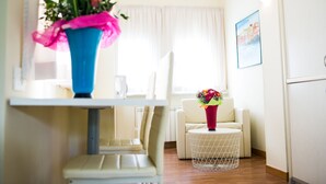 A modern living room with a dining area, featuring a blue vase with flowers, a white sofa, and a small round table. - Rex Hotel Residence (Genoa)