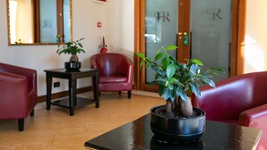A reception area with a potted plant on a table, a red chair, and a mirror on the wall. - Rex Hotel Residence (Genoa)
