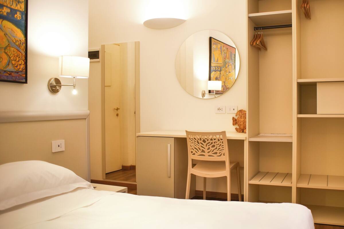 Une chambre d’hôtel comprenant un lit, un bureau, une chaise, une armoire et un miroir.