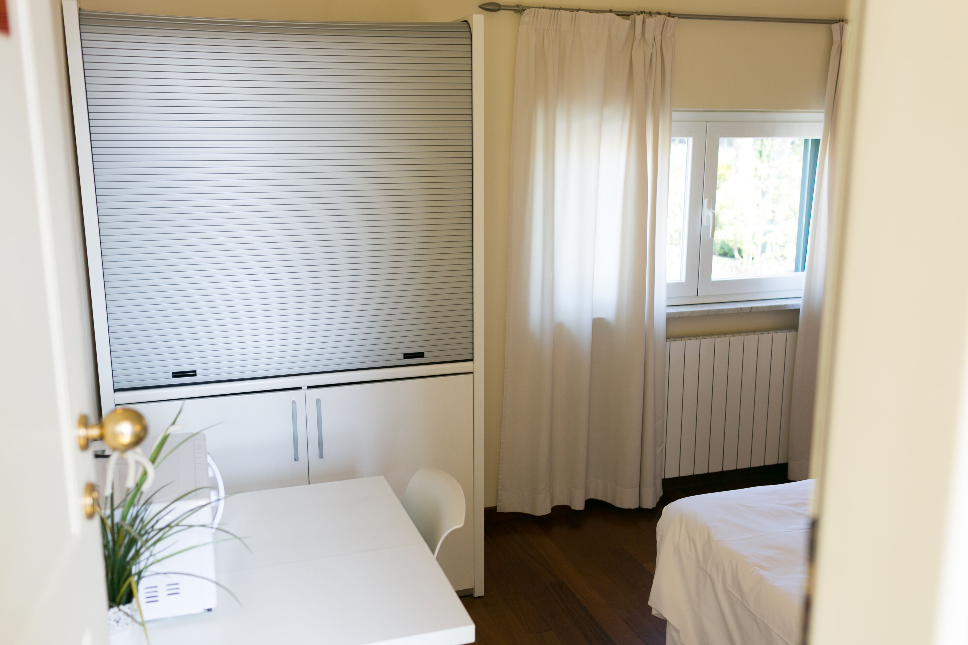 Une chambre avec un lit, un bureau et une fenêtre avec des rideaux.
