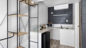 Eine kleine Küche mit weißen Schränken, einem schwarzen Kühlschrank und einer Mikrowelle auf der Arbeitsfläche.
