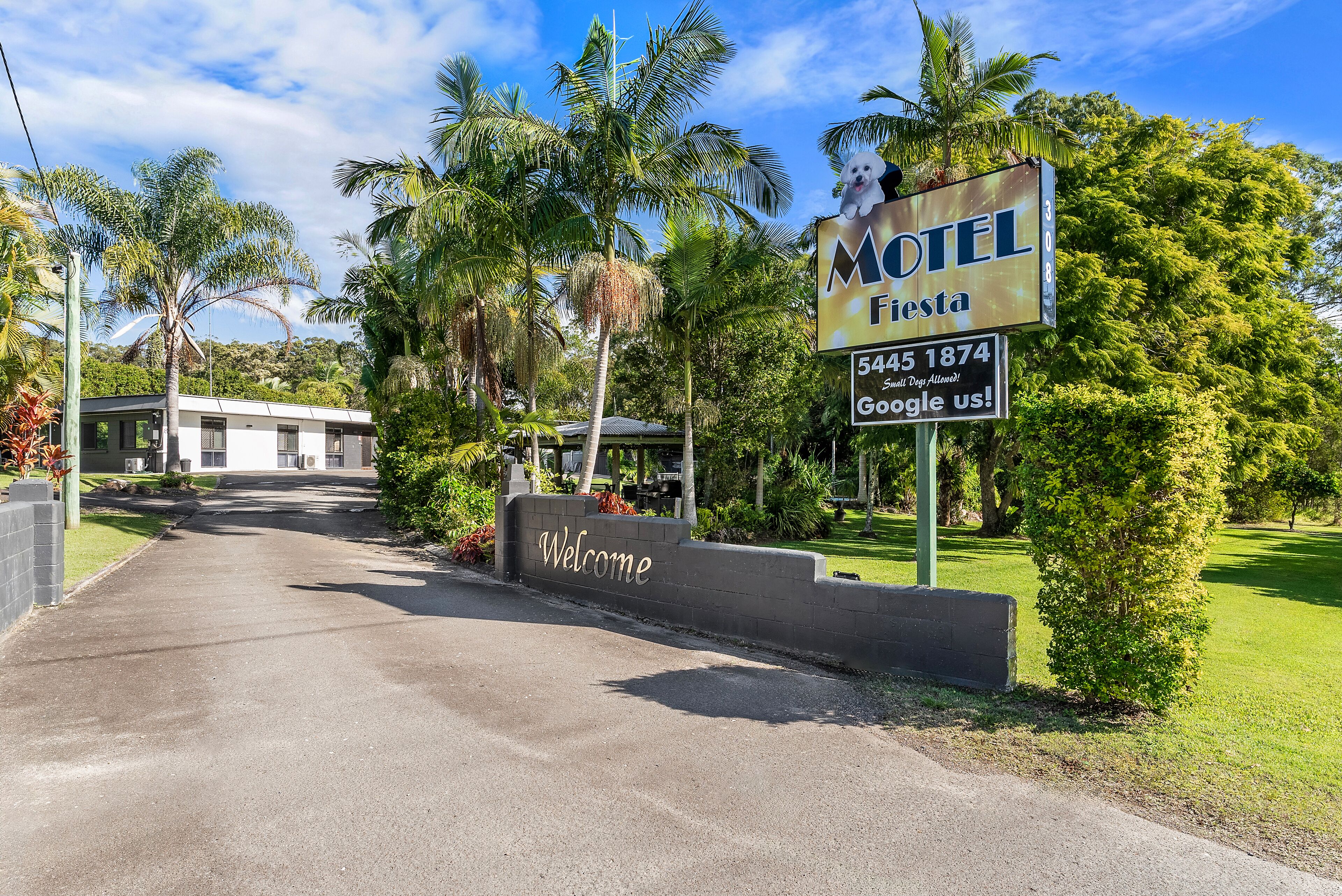 L’entrée d’un motel, avec une pancarte « Bienvenue », des palmiers et un ciel dégagé.