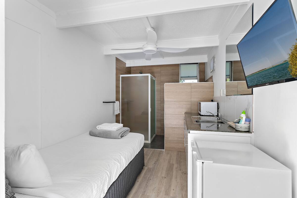 Moderni hotellihuone, jossa on sänky, työpöytä, televisio ja suihkutila.