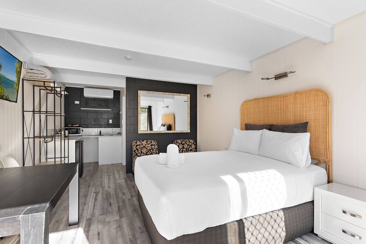 Moderni hotellihuone, jossa on suuri sänky, työpöytä ja pieni keittiönurkkaus.