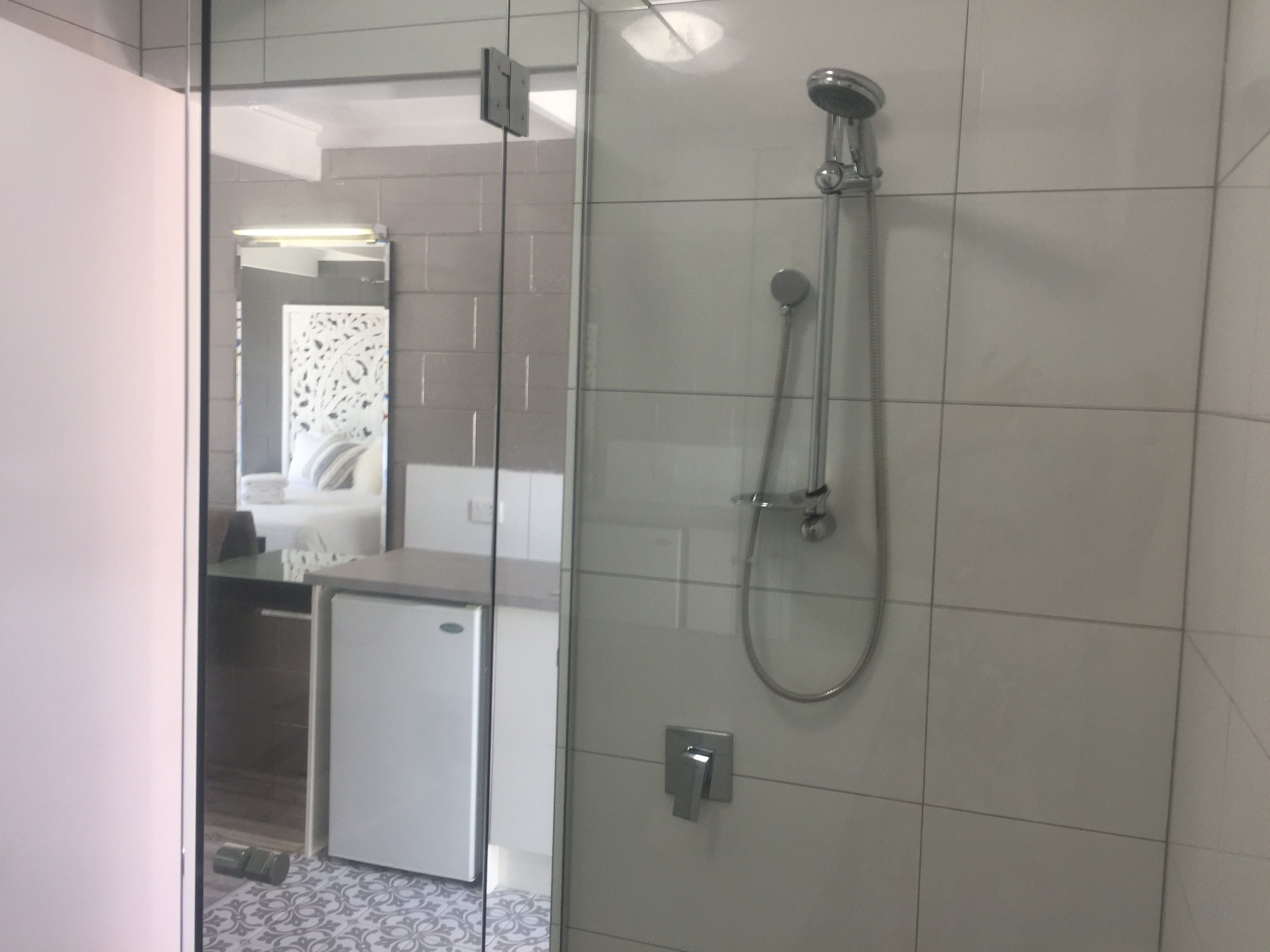 A modern bathroom with a glass shower enclosure, a small white cabinet, and a patterned floor.