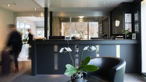 A modern reception area with a reception desk, a black leather chair, and two potted orchids. - Jungfrau Hotel (Wilderswil)