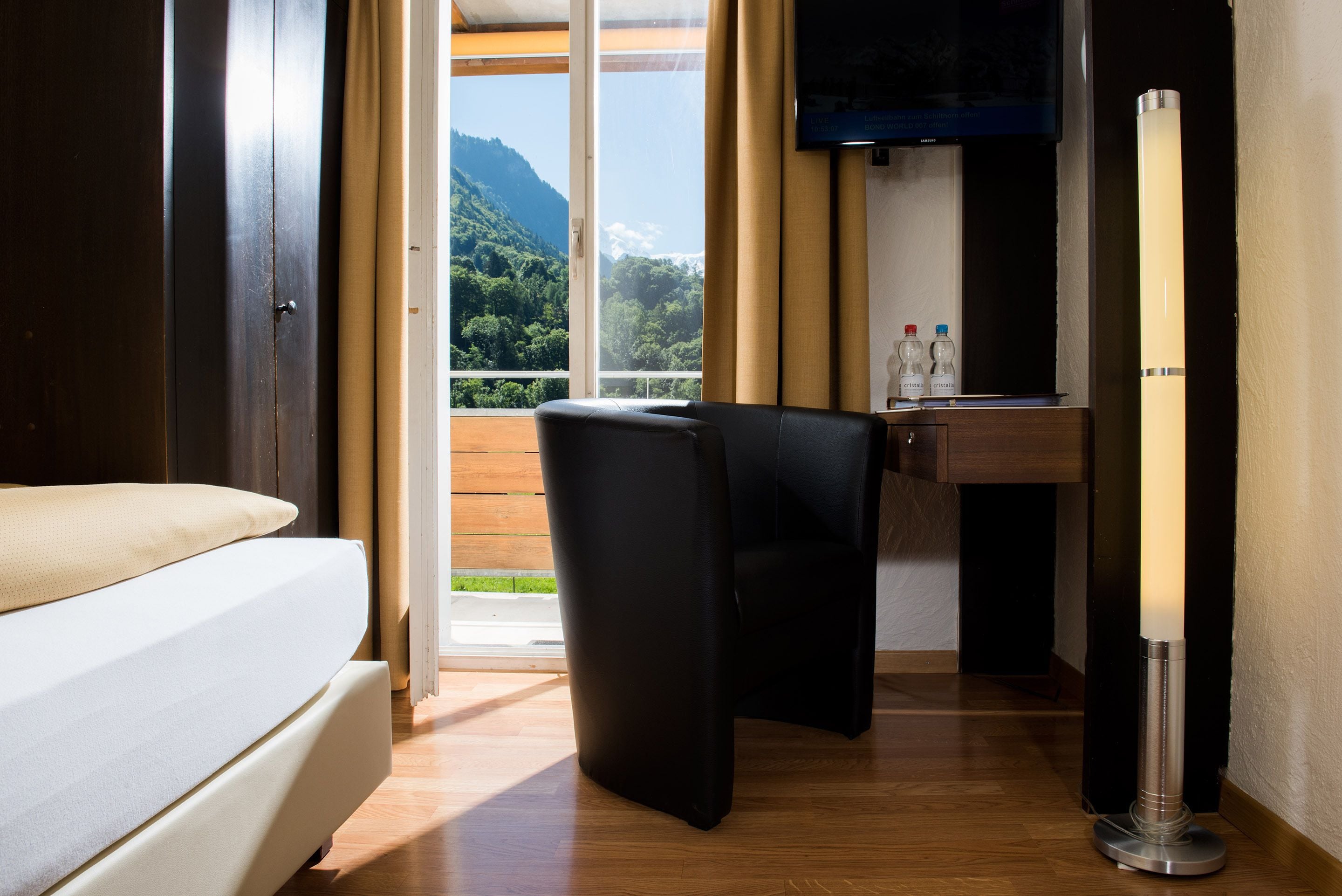 A hotel room with a bed, a desk, a chair, a TV, and a view of mountains.