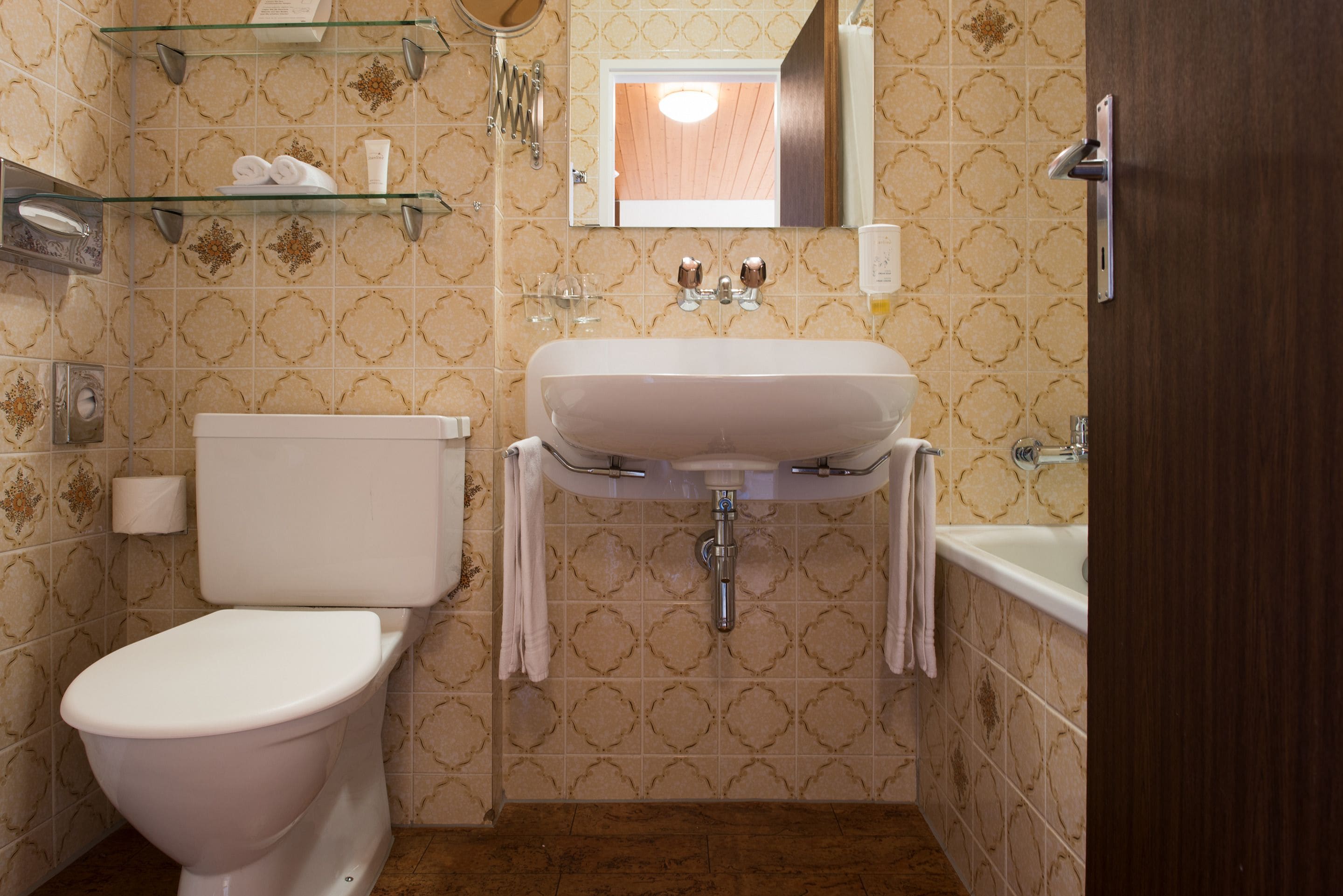 A bathroom with a toilet, sink, and bathtub. There are towels on the wall and a mirror above the sink.