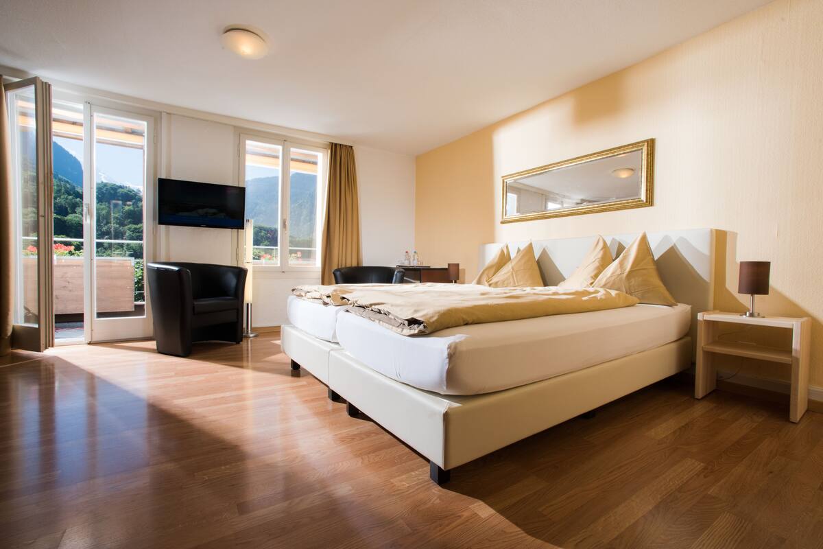 Quarto espaçoso com uma cama grande, televisão e porta de vidro deslizante para uma varanda.