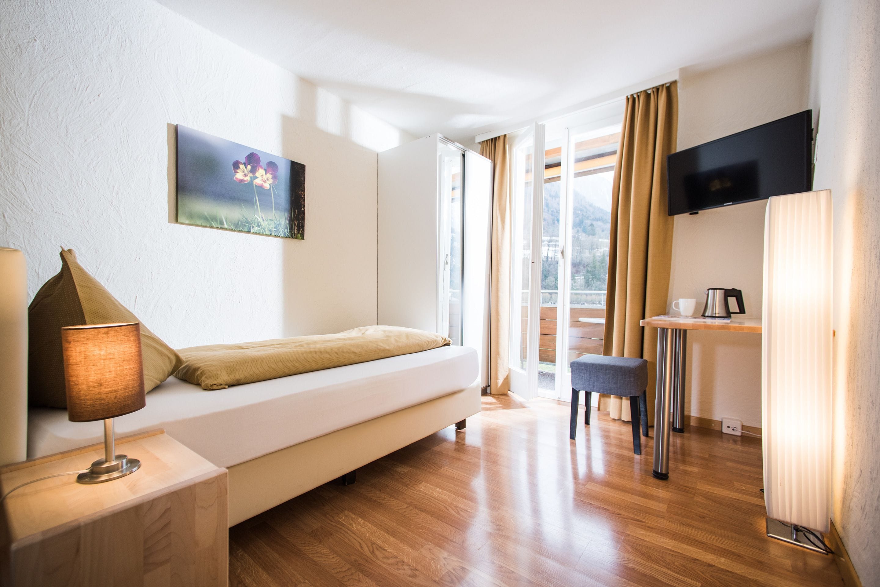 A modern hotel room with a sofa bed, a desk with a chair, a flat-screen TV, and a painting on the wall.