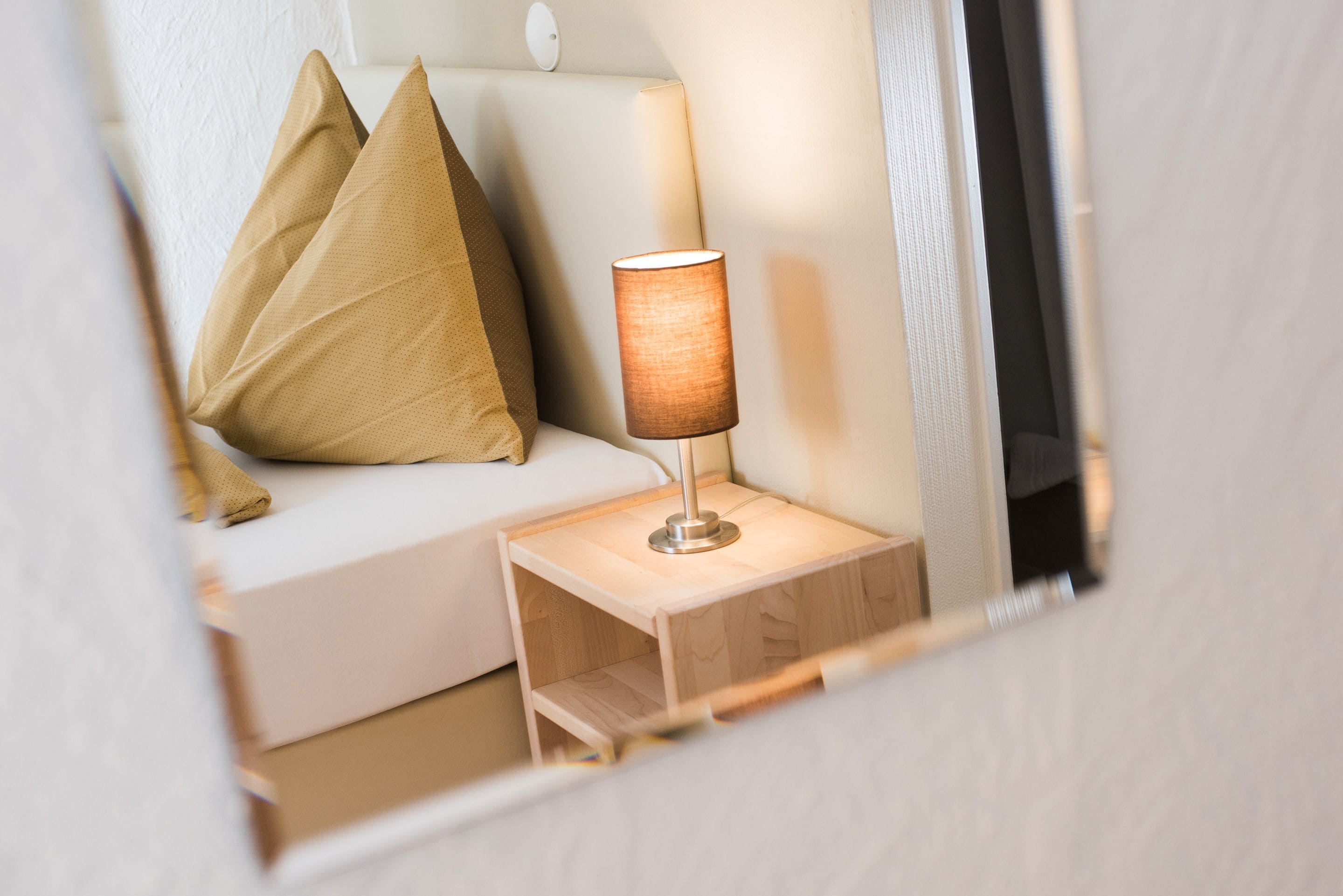 A neatly arranged bedroom with a bedside table, a lamp, and two pillows on a white sofa.